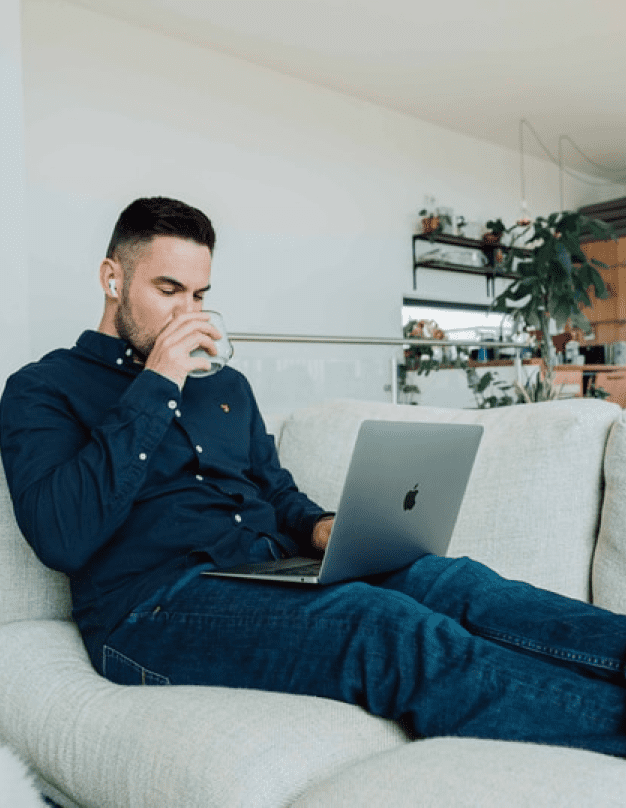 画像:グレーのソファーの上でパソコンを足の上に載せくつろぐ男性